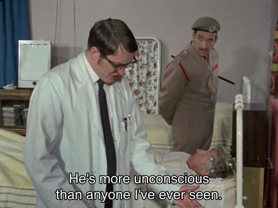 Jon Pertwee episode. The Doctor is wearing a white hospital gown and several weird silver orbs on his head, lying down in a bed under a pastel yellow striped blanket, extremely unconscious, evidently. The Brigadier is standing by his side, big boy stick under his left arm, looking at a doctor (the regular kind) on the other side, a man with excellent glasses, looking over some paperwork offscreen. Caption reads, “He’s more unconscious than anyone I’ve ever seen.” I didn’t know there were so many levels of unconscious.