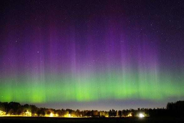 A night sky filled with dancing curtains of intenced green and red aurora borealis covering the whole sky above the horizon.