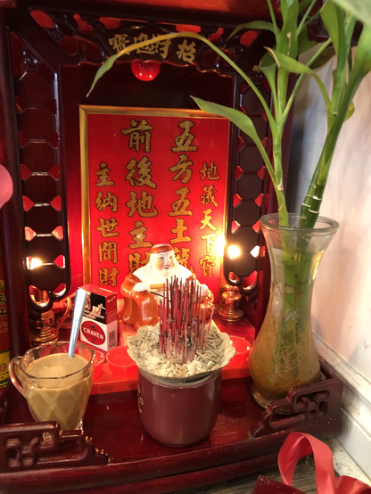 dark red wooden structure contains several items, including a small white figurine and a green plant in a clear glass vase. A red background panel displays vertical gold Chinese characters: 