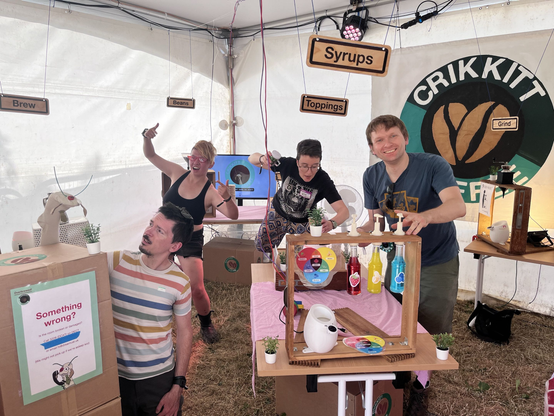 Five people are in a café-themed escape room. The room is full of stations (syrups, toppings, grinding beans). There is a sock puppet cricket.