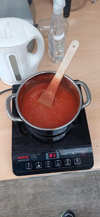 A large stainless-steel saucepan filled with homemade tomato sauce simmering on a portable induction hob, with a wooden spoon resting in the pot.