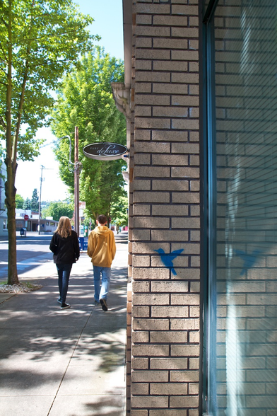 2 people walking past a brick wall with a painted bird on it