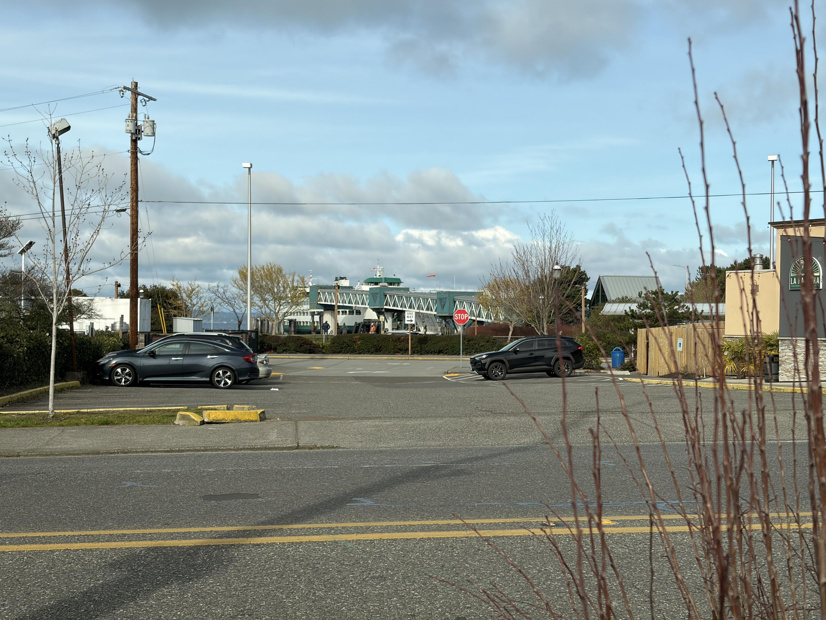 Two cars parked in a lot near a ferry terminal under a partly cloudy sky.