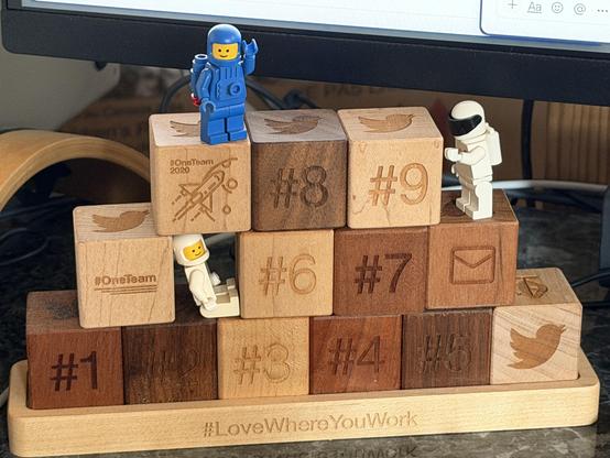 A stack of wooden blocks, with various Twitter symbols and emoji. There are numbers, 1-9, representing years of service. The blocks are stacked in 3 rows, and have lego space mini-figures playing on them.