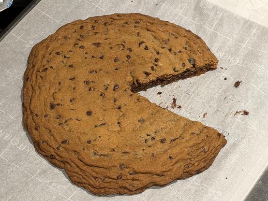 Dinner plate-sized chocolate chip cookie with a section cut out of it resembling Pac-Man