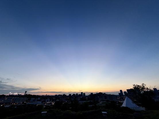 a wide angle view of the sunset over a city, with rays of light from the center of the image
