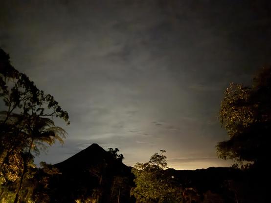 A tropical twilight scene, with a large dark  mountain shape in the background, a volcano 