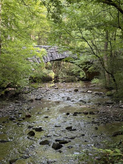 An old stone bridge, in the great Smoky Mountains National Park, passing over water and surrounded by deep summer foliage.