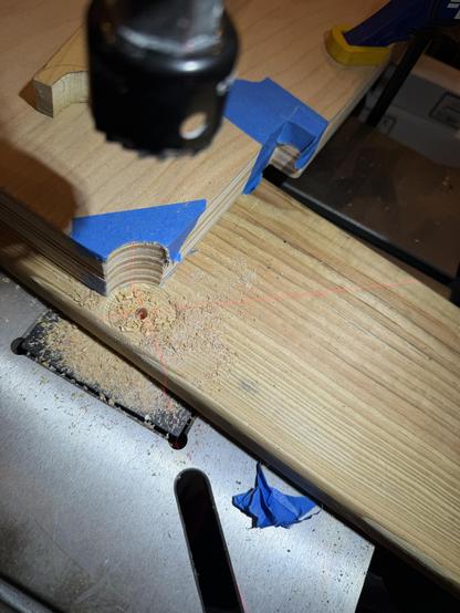 A drill press with a circular Cutting bit over a sandwiched piece of plywood which has had a notch cut out of it. There’s a red laser X projected directly over the hole.